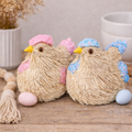 Pink and blue straw chicken decorations with floral and polka dot fabric caps and wings sitting side by side on a timber surface with pastel Easter eggs and a wooden bead garland — Mistletoe Home