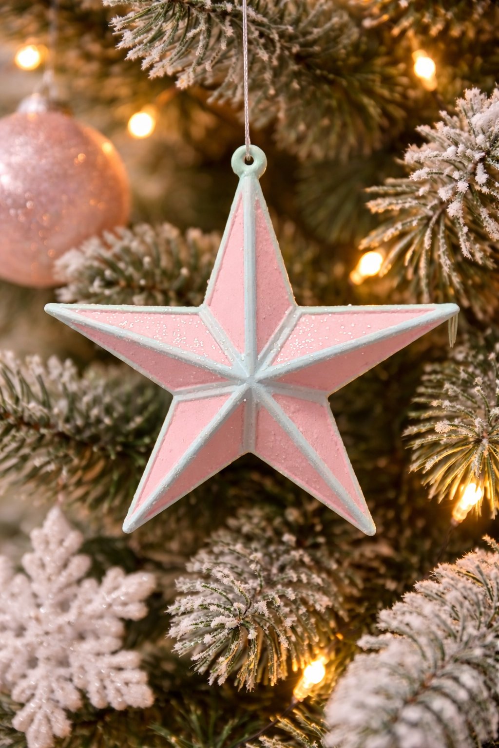 Pink glitter and mint-blue 3D star Christmas ornament hanging on a frosted Christmas tree with warm fairy lights and pink bauble — Mistletoe Home