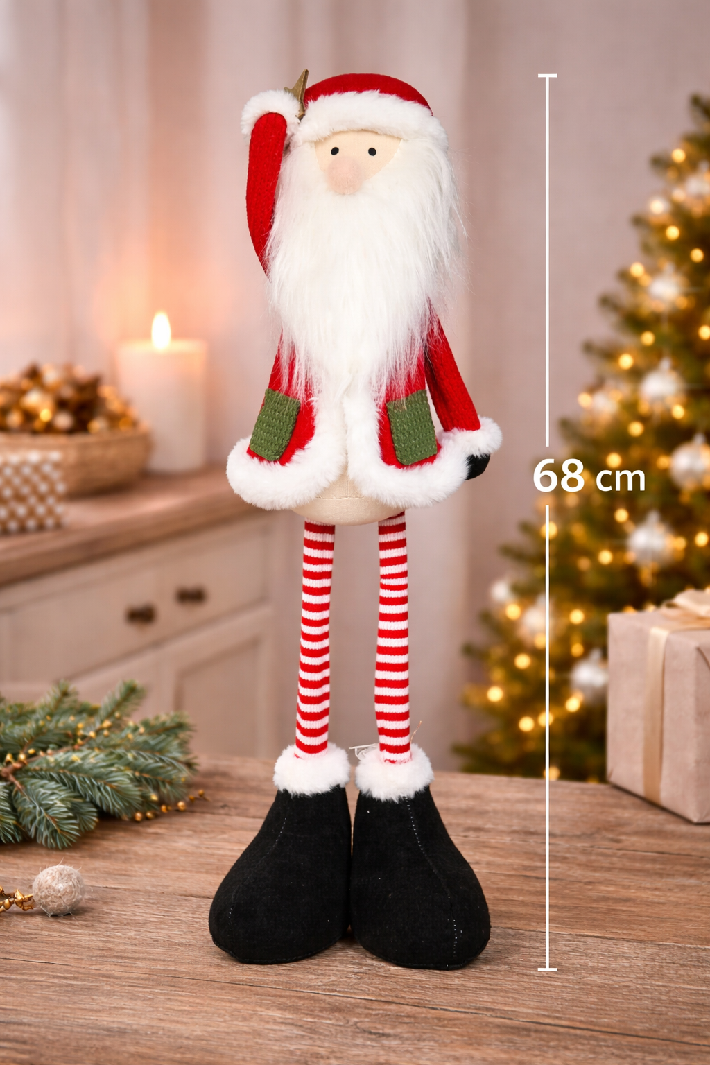 8cm standing fabric Santa decoration with fluffy white beard, red coat, green pockets, candy-striped legs and black boots styled on a timber surface with a Christmas tree, candle and wrapped gifts in the background — Mistletoe Home