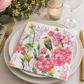 Watercolour garden bird and floral napkin folded on a white plate with pink peonies, candle and wine glass at a table setting