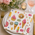 Sweet treats print napkin folded on a white plate with pink florals, candle and glass of rosé at a table setting