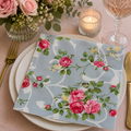 Vintage blue rose trellis napkin folded on a white plate with pink roses, candle and glass of rosé at a table setting
