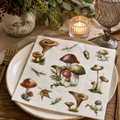 Woodland mushroom napkin folded on a rustic plate with a mushroom-print vase, pine and berry sprigs, and a candle at a table setting