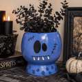 Blue Frankenstein ceramic planter with stitched face on a mantel, holding black faux eucalyptus stems beside black candles and a white pumpkin