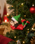 Daydreaming elf Christmas ornament hanging on a tree branch beside red and gold baubles with fairy lights