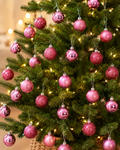 Pink Christmas baubles hanging on a decorated tree, mix of matte, glitter and glossy finishes with warm fairy lights