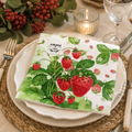 Watercolour strawberry vine napkin folded on a white plate with rattan charger, red berries and a candle at a table setting