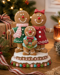 Gingerbread family Christmas figurine displayed on a wooden table in front of a lit Christmas tree, with wrapped gifts and a lantern in the background
