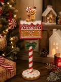 Gingerbread mailbox Christmas figurine displayed on a wooden table beside a gift box, Christmas tree, and gingerbread houses