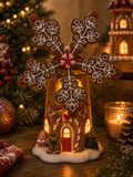 Light-up gingerbread snowflake house figurine displayed on a wooden table beside a Christmas tree and gingerbread houses