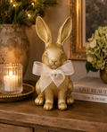Gold bunny figurine with white organza bow displayed on a wooden console table beside a candle and hydrangeas