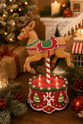 Light-up gingerbread reindeer carousel figurine displayed on a wooden table with candles, gifts, and a gingerbread house in the background