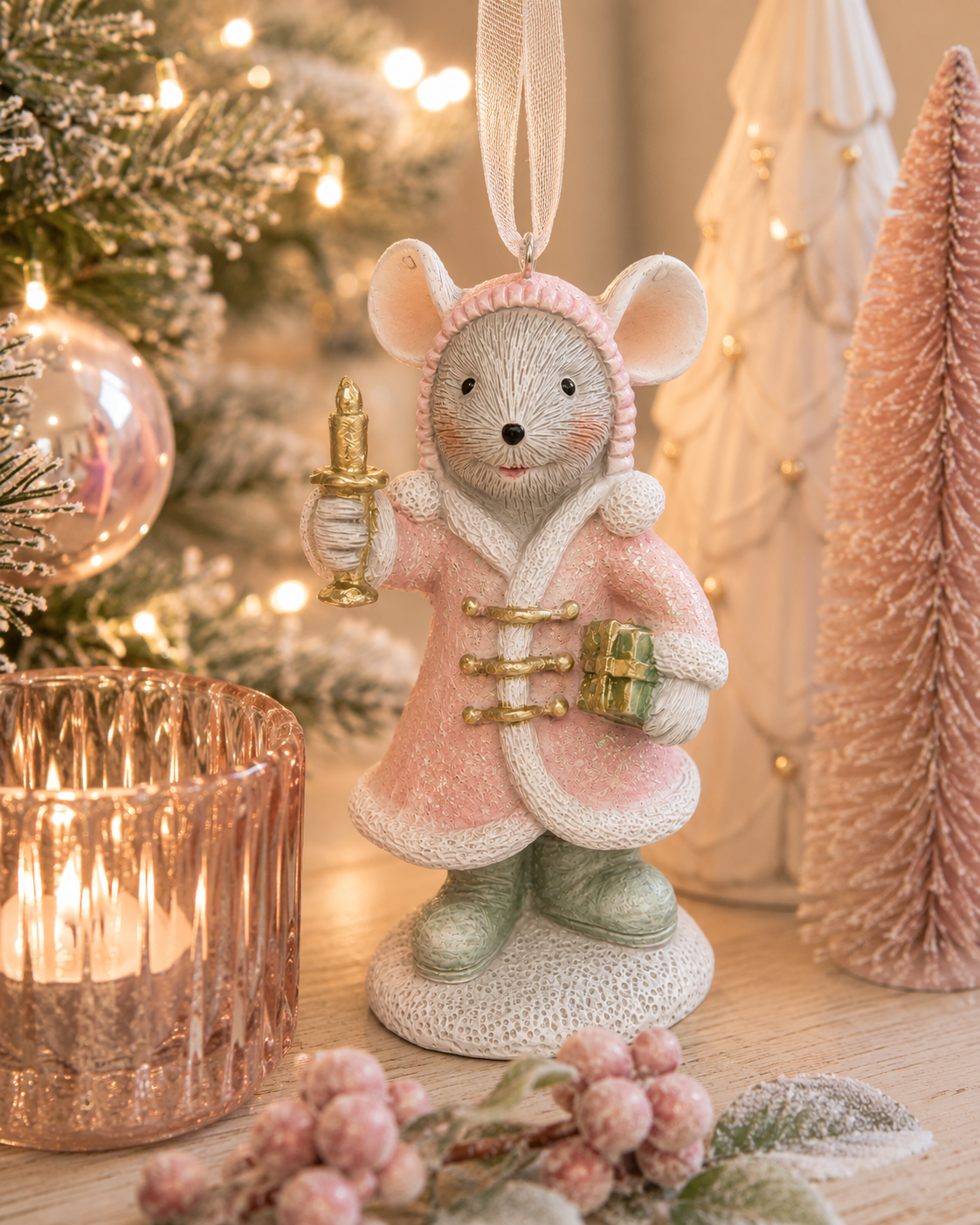 Pink cloak mouse with candle and gift hanging ornament displayed on a table beside a lit tree, bottle brush trees, and pink baubles