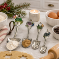 Succulent garden charm measuring spoon set displayed on a marble kitchen bench beside flour, eggs, and gingerbread dough