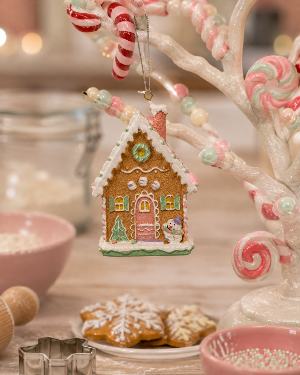 Pastel gingerbread house hanging ornament displayed on a candy cane tree branch beside lollipops