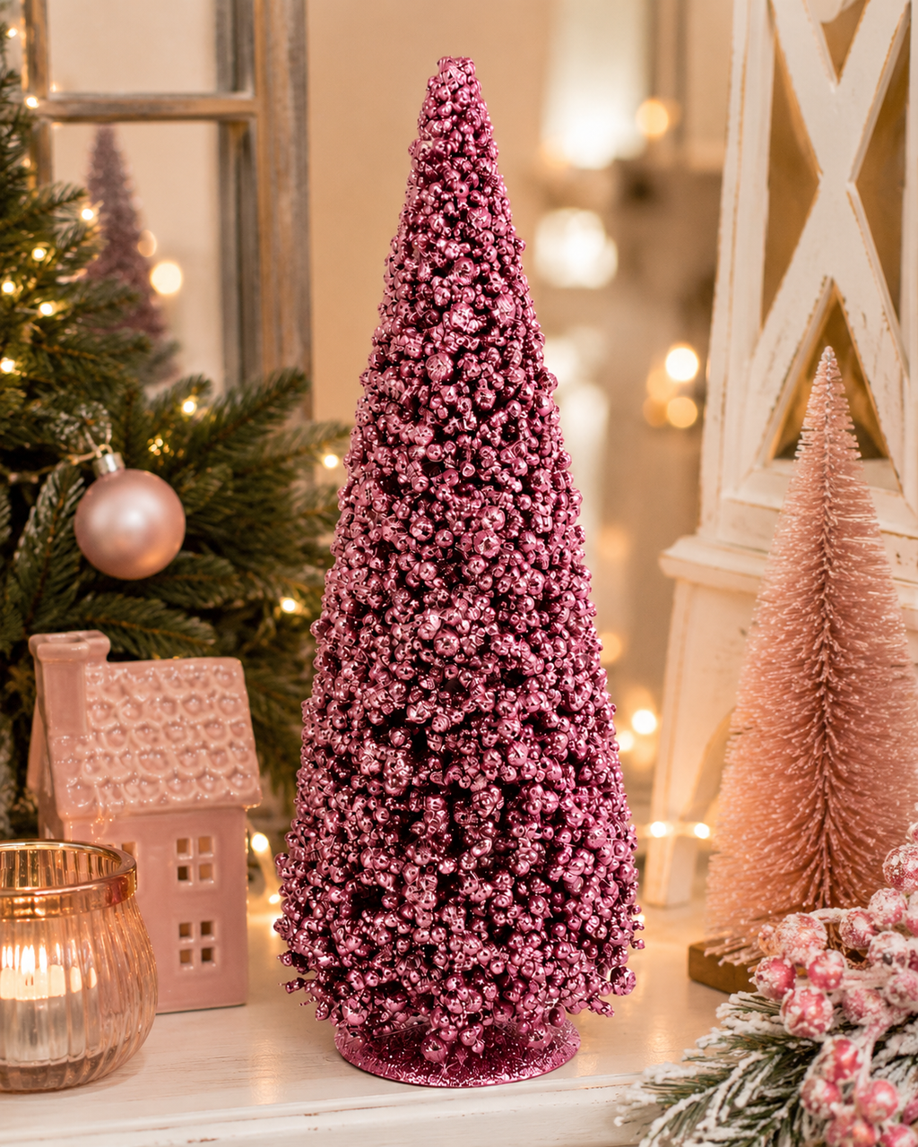 Pink beaded cone Christmas tree displayed on a mantel beside a pink ceramic house, candle, and bottle brush trees