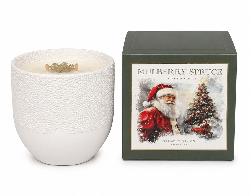 Mulberry Spruce luxury soy candle in a white textured ceramic vessel next to its dark green gift box featuring a Bramble Bay Co Santa and sleigh illustration