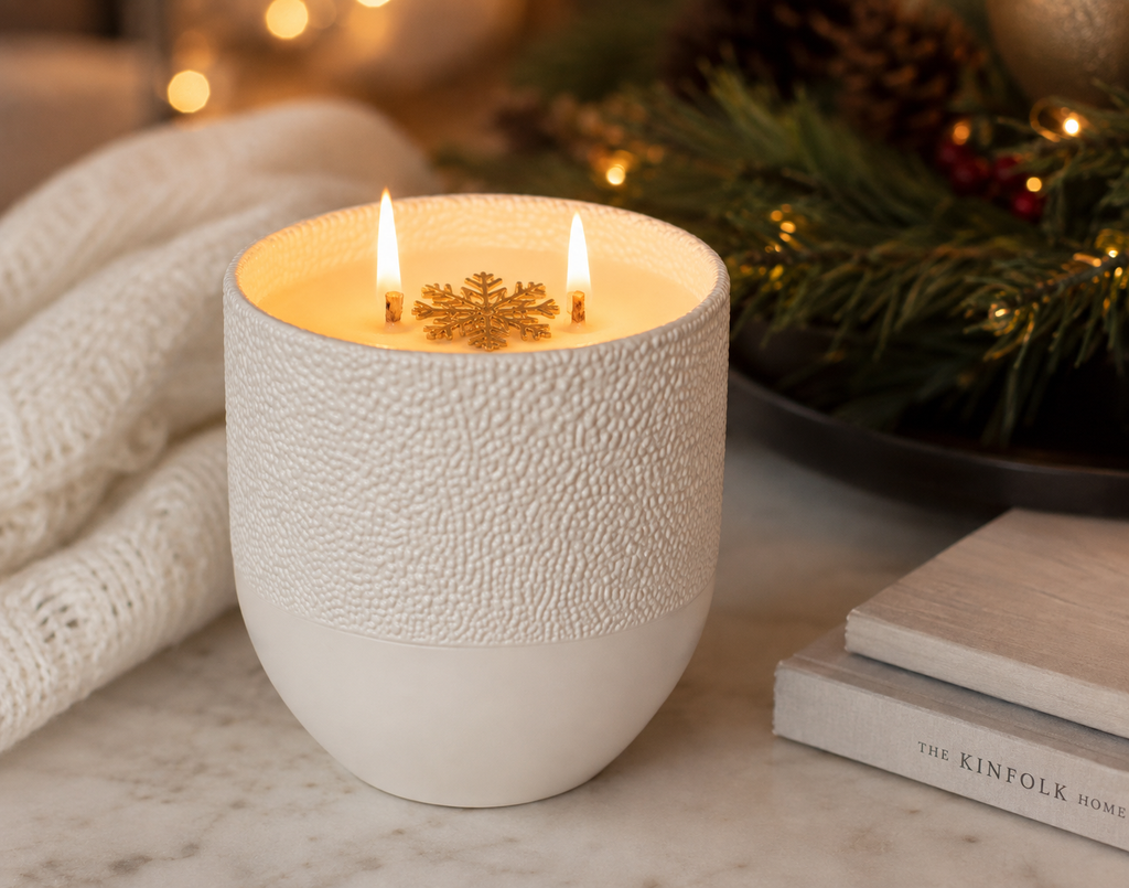 Cinnamon & Spice soy candle burning with two lit wicks on a marble surface, styled with a cream knit throw and Christmas garland with fairy lights in the background
