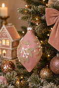 Silver mistletoe beaded glass long drop ornament hanging on a Christmas tree, near a lit candle and a mini gingerbread house decoration