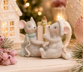 Christmas Gift-Giving Mice Duo Figurine displayed on a table beside a lit house ornament and frosted pink berries, with warm bokeh lights in the background