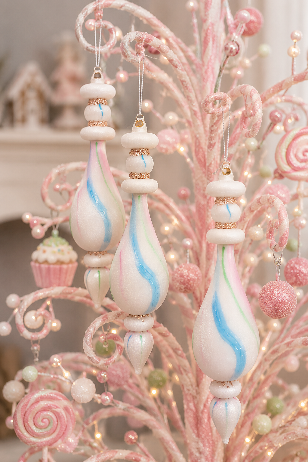 Pastel watercolour glass finial ornaments hanging on a pink candy-themed Christmas tree, showing the frosted white glass with pink, blue and mint swirl detailing and rose gold glitter bands