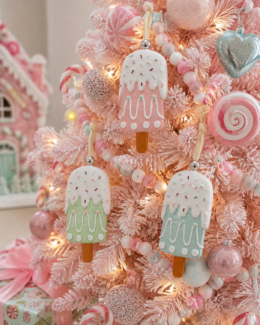 Pastel popsicle Christmas ornaments hanging on a pink flocked tree among candy and pastel baubles with fairy lights