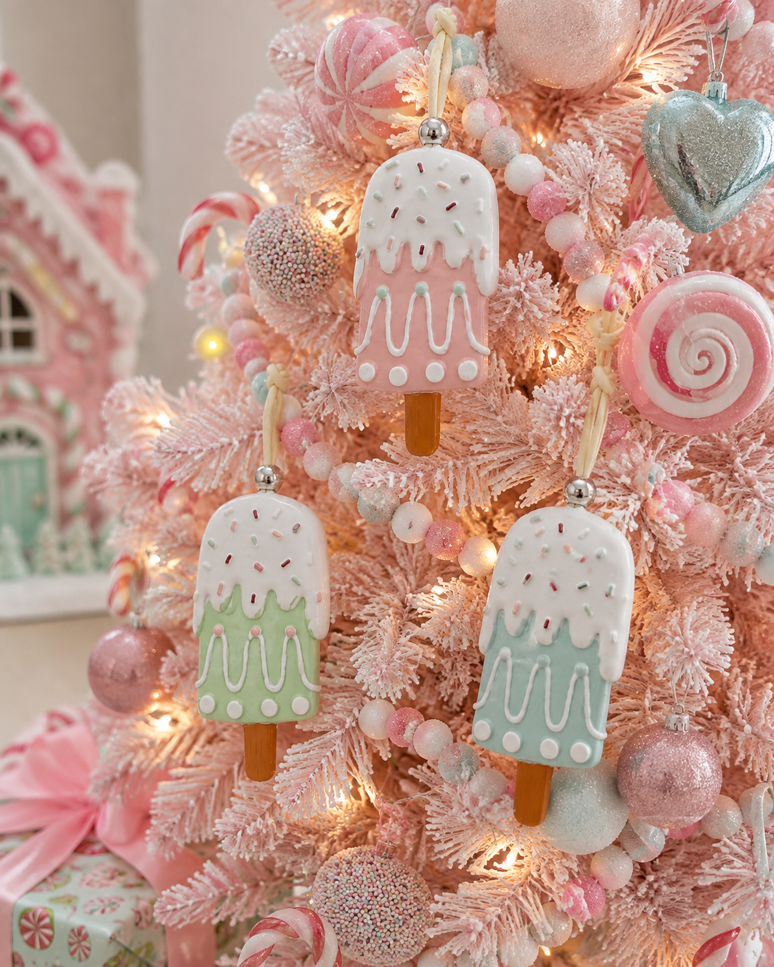 Pastel popsicle Christmas ornaments hanging on a pink flocked tree among candy and pastel baubles with fairy lights