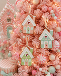 Pastel gingerbread house Christmas ornaments hanging on a pink flocked tree beside candy decorations and peppermint baubles