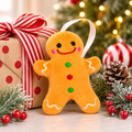 Plush gingerbread man Christmas ornament standing beside a wrapped gift with a striped ribbon bow, pine and holly berrie