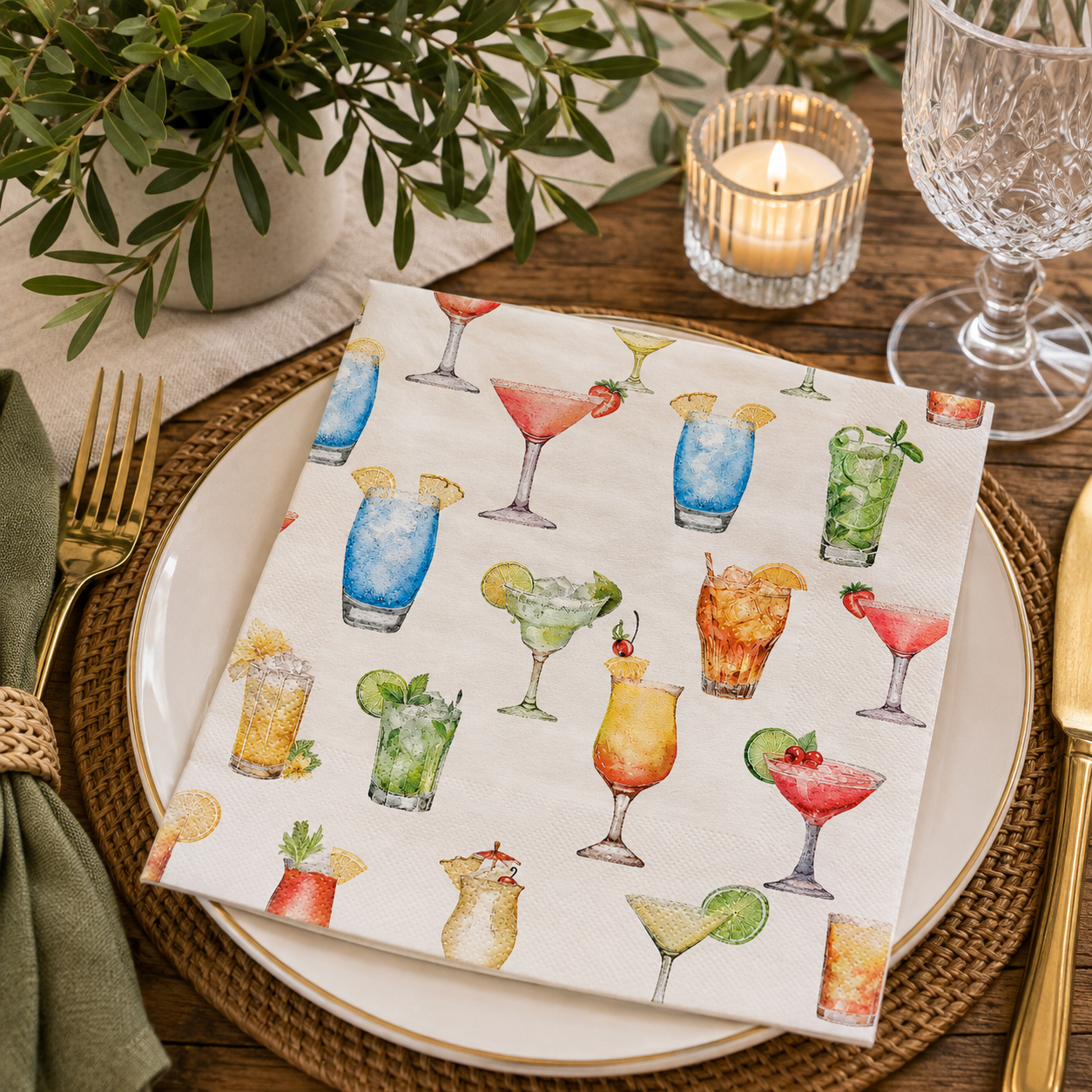 Watercolour cocktail print napkin folded on a plate with greenery, candle and wine glass at a table setting