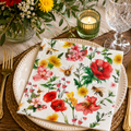 Watercolour bee and wildflower napkin folded on a white plate with a floral arrangement, green candle holder and wine glass at a table setting