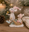 Mouse and sleigh Christmas figurine on a wooden surface, mama mouse in a pink knitted hat ringing a gold bell and pulling a baby mouse in a glittery gold sleigh, styled with a candle, pinecone and frosted greenery.
