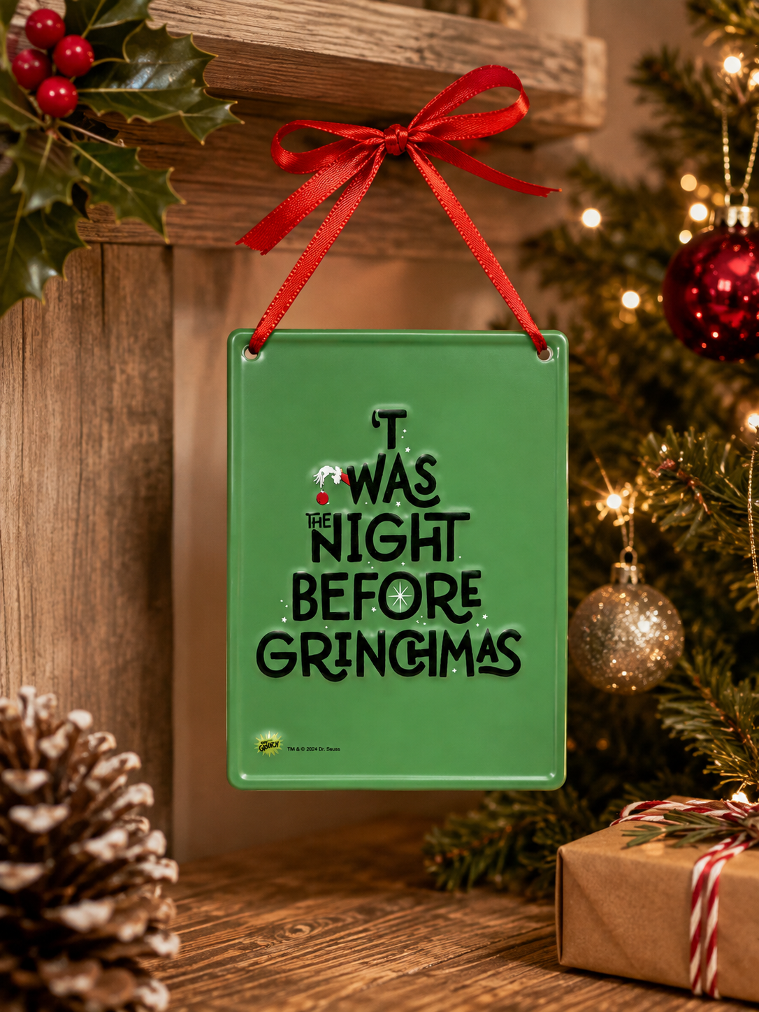 'T Was the Night Before Grinchmas tin hanging sign on a wooden shelf with holly, pinecones and a wrapped gift near a Christmas tree