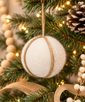 White felted wool ball ornament wrapped in jute cord hanging on a Christmas tree, styled with a snowy pinecone, wood bead garland, and burlap ribbon