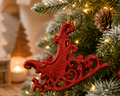 Red glitter filigree sleigh ornament hanging on a Christmas tree, styled with a snowy pinecone and warm fairy lights