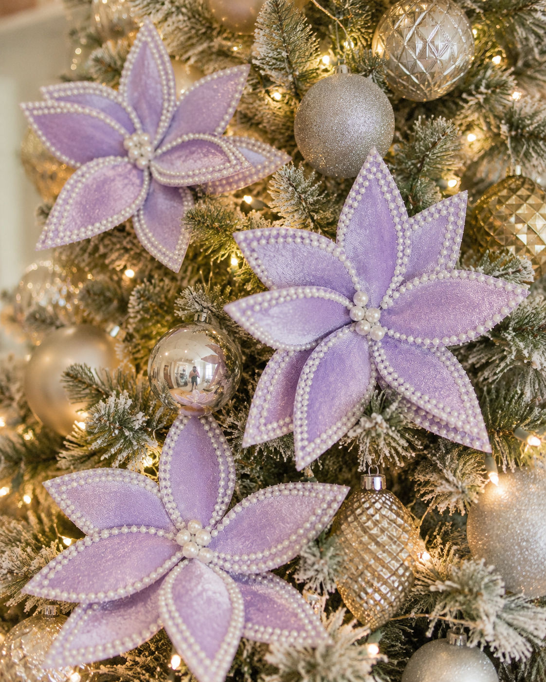 Purple poinsettia picks with pearl trim clustered on a flocked Christmas tree, styled with gold and silver glitter baubles and warm fairy lights