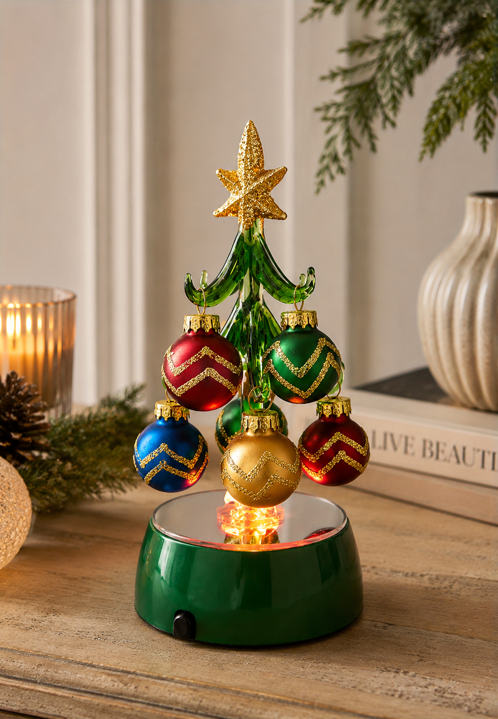 Light-up glass Christmas tree with mini baubles glowing on a wooden console table, beside a candle, pinecone and ceramic vase