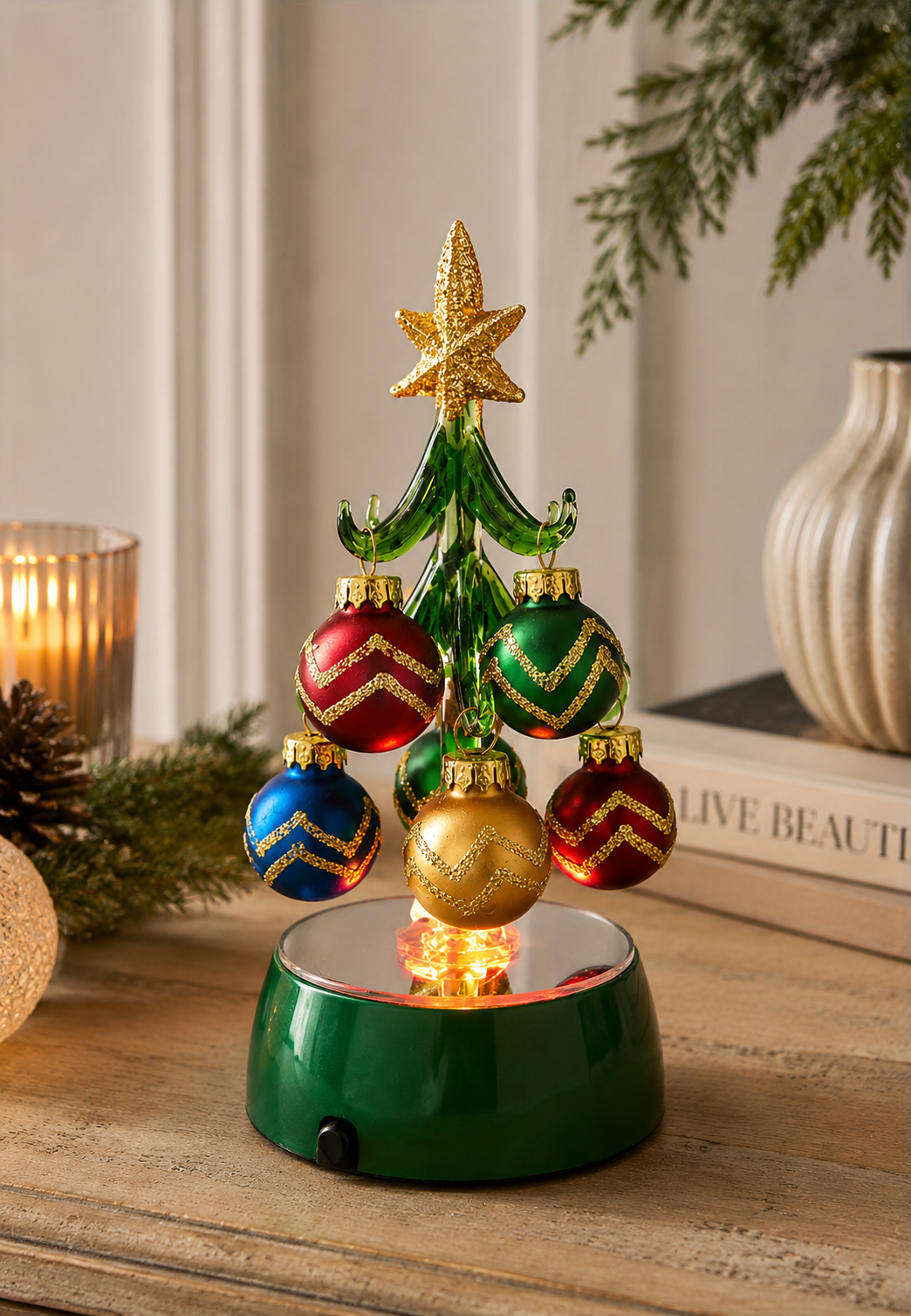 Light-up glass Christmas tree with mini baubles glowing on a wooden console table, beside a candle, pinecone and ceramic vase