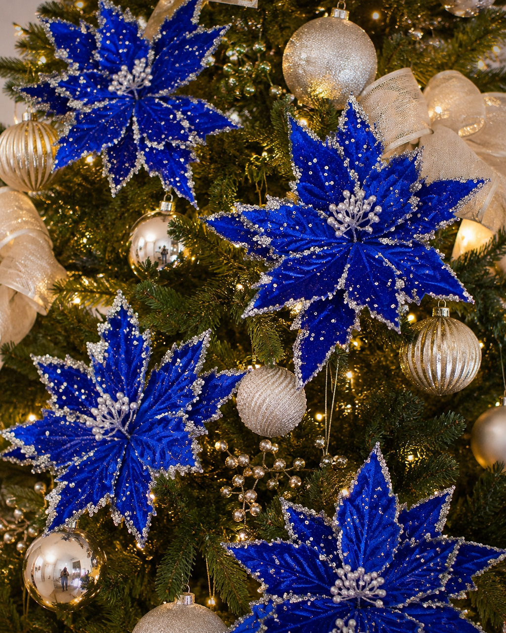 Dark blue poinsettia picks with silver glitter edging clipped throughout a Christmas tree among gold baubles and sheer ribbon