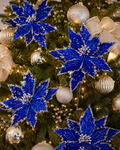 Dark blue poinsettia picks with silver glitter edging clipped throughout a Christmas tree among gold baubles and sheer ribbon