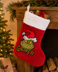 Grinch Christmas stocking hanging from a wooden mantel decorated with pine and berries, filled with a candy cane and wrapped gifts, red plush with white fur cuff and embroidered Grinch face.