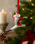 Nutcracker Rat King ornament hanging on a Christmas tree beside a lit candle, pinecones, and a wrapped gift with a red velvet bow
