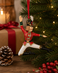 Nutcracker Prince ornament hanging on a Christmas tree beside a wrapped gift, pinecone, and red berry sprigs