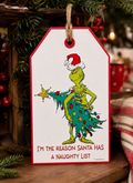 Grinch naughty list hanging sign displayed on a wooden crate surrounded by pine branches and berries, red mug and plaid blanket in background, Grinch wrapped in Christmas tree with "I'm the reason Santa has a naughty list" text.