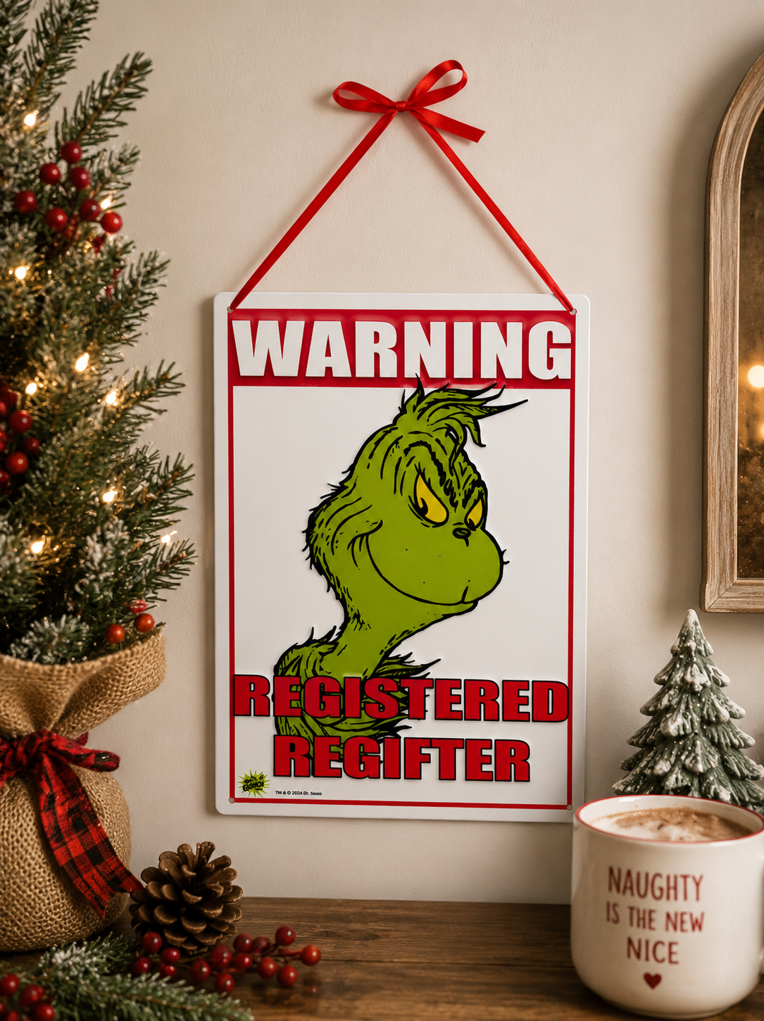 Grinch "Registered Regifter" tin sign hanging on a wall beside a Christmas tree, styled with pinecones, berries and a "Naughty is the New Nice" mug