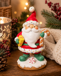 Sprinkle Santa gingerbread figurine on a wooden table styled with a lit lantern, pine sprigs and red berries in a warm holiday scene.