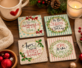 Set of four Christmas quote ceramic coasters on a wooden table styled with a heart-print mug, lit candle, pinecone and bowl of baubles.