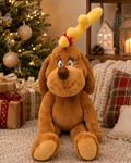 Max plush toy, the Grinch's dog, sitting under a Christmas tree with wrapped gifts and plaid cushions, wearing his yellow antler tied with a red ribbon