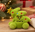 Grinch Christmas tree mini plush sitting on a wooden surface near a Christmas tree and wrapped gifts, showing gold star topper and embroidered ornament dots