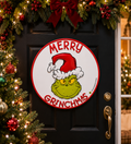Merry Grinchmas round door sign hanging on a black front door, surrounded by Christmas garland, red bow, and berries